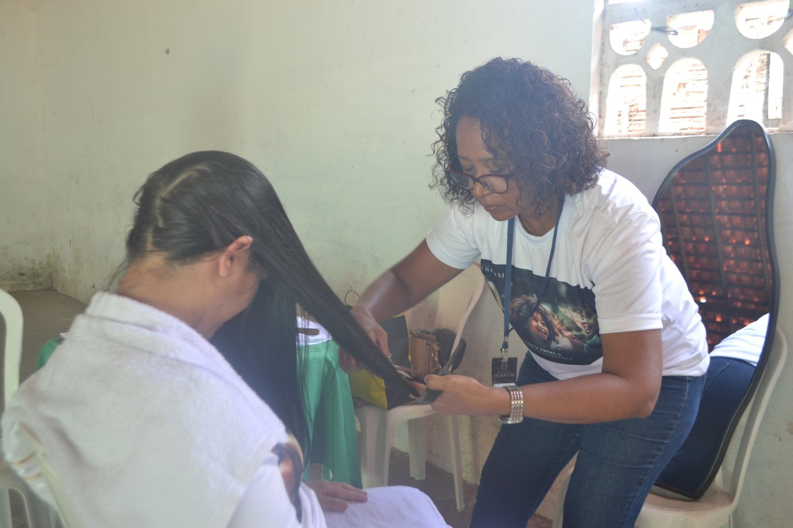 Voluntária do Instituto Hebrom fazendo um alisamento de cabelo em uma moradora durante o Dia D Hebrom no bairro da Matinha, São Luís